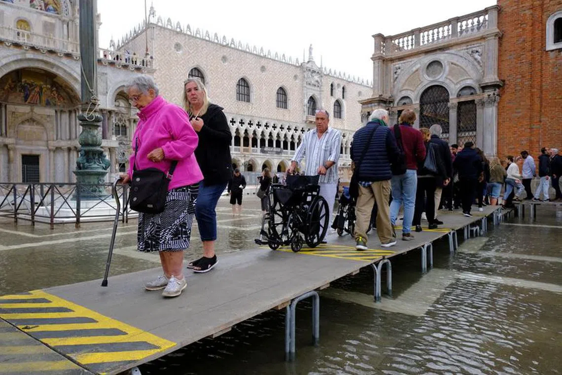 People walk on a catwalk at the flooded St. Mark's Square during seasonally high water in Venice, Italy, September 28, 2022. REUTERS/Manuel Silvestri/File Photo