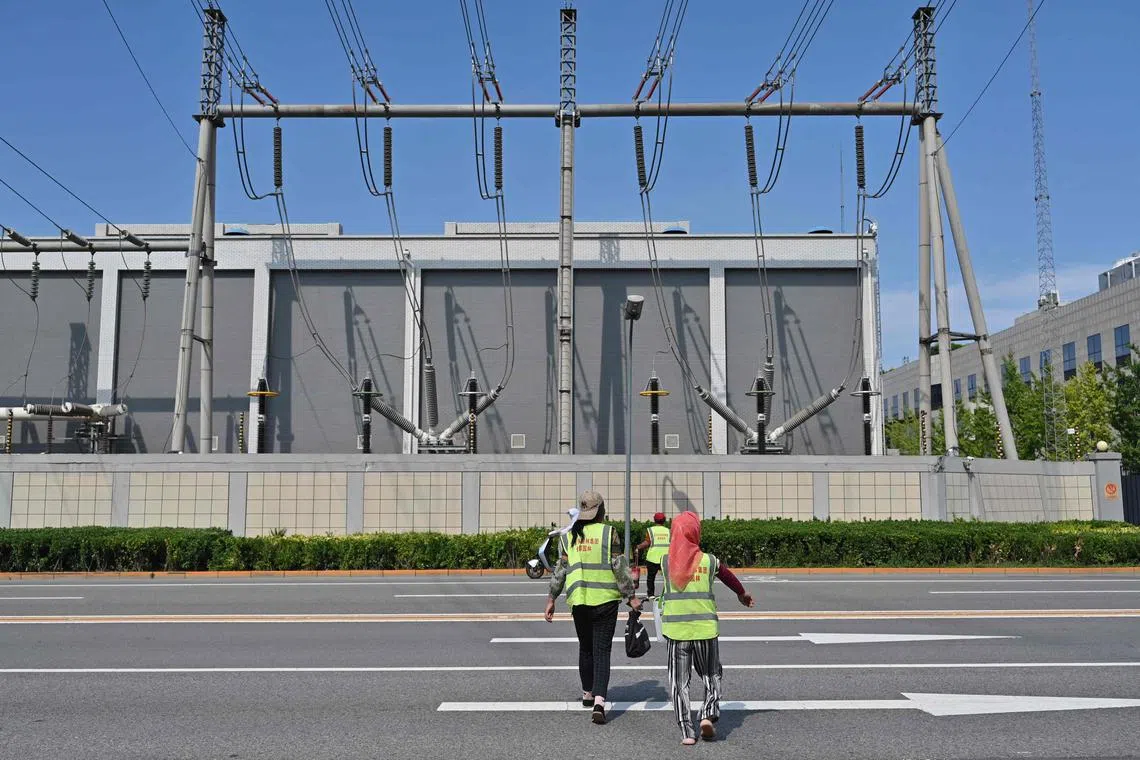 Workers cross a road in front of electricity installations in Beijing on July 31, 2024.
