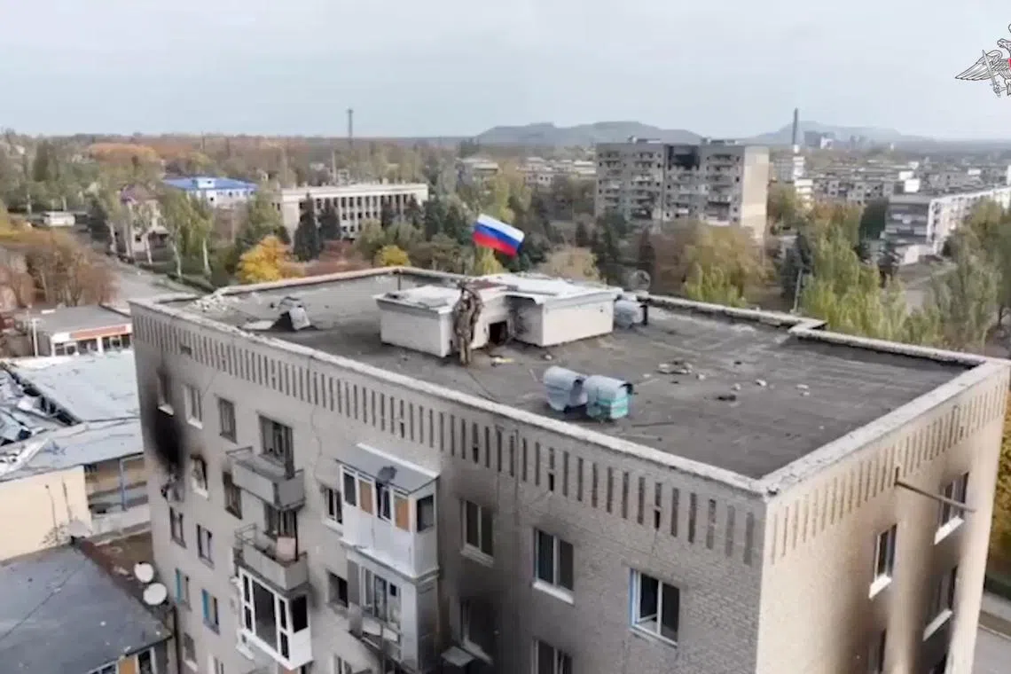 Russian service members hoist a Russian flag on the top of a building in Selydove, after Russian forces captured the town in Ukraine's eastern Donetsk region.