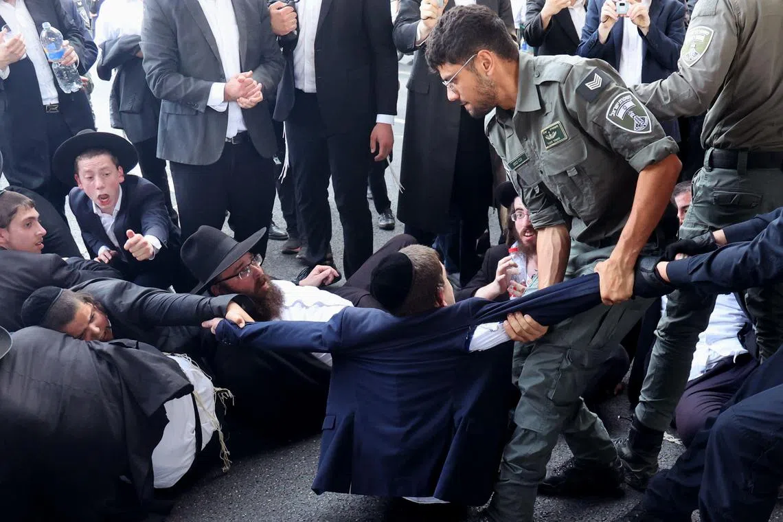 Israeli police remove a protester as they disperse Ultra-Orthodox Jews blocking a highway during a protest against possible changes regarding the laws on the military draft from which the Ultra-Orthodox community has traditionally been exempt, in the central Israeli city of Bnei Brak, on June 20, 2024, amid the ongoing conflict between Israel and the Palestinian Hamas militant group. Israel's High Court of Justice unanimously ruled on June 25 that the state "must" draft ultra-Orthodox Jewish men to military service, a decision that could upend Prime Minister Benjamin Netanyahu's ruling coalition. (Photo by JACK GUEZ / AFP)