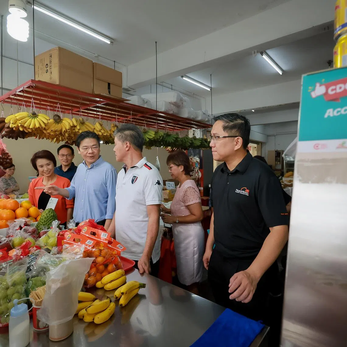 DPM Lawrence Wong (centre, in blue) speaking with a fruit stall owner (in white) with mayors (from left) Low Yen Ling, Desmond Choo, Denise Phua and Alex Yam at the CDC Vouchers Scheme launch on Jan 3.