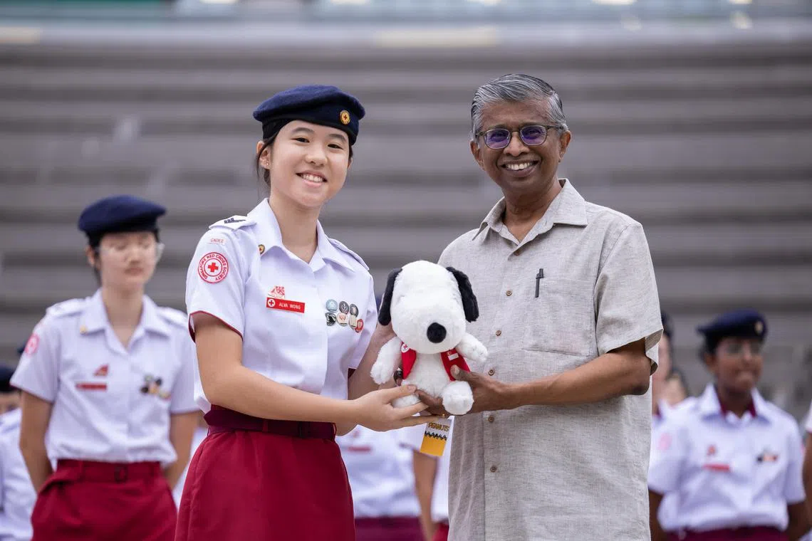 ST20250415_202573400574/JKCPR20/Brian Teo/Joakim Kang/(From left) Alva Wong, 16, a secondary four student at Raffles Girls' School, receiving a Snoopy plush dressed in a Singapore Red Cross vest from Mr Benjamin William, secretary general and CEO of the Singapore Red Cross, during morning assembly at the school campus on April 15, 2025. Alva was recognised for performing CPR on a tourist suffering from cardiac arrest, helping to save their life before SCDF personnel arrived. ST PHOTO: BRIAN TEO 