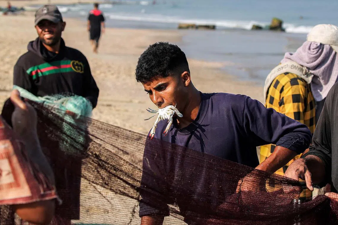 TOPSHOT - A fisherman holds a crab in his mouth as he pulls in a net to shore along a beach in the Nuseirat camp for Palestinian refugees in the central Gaza Strip on August 30, 2025. The Israeli military declared Gaza City "a dangerous combat zone" on August 29 ahead of its military operation in the Palestinian territory's largest city after almost two years of devastating war. (Photo by Eyad BABA / AFP)