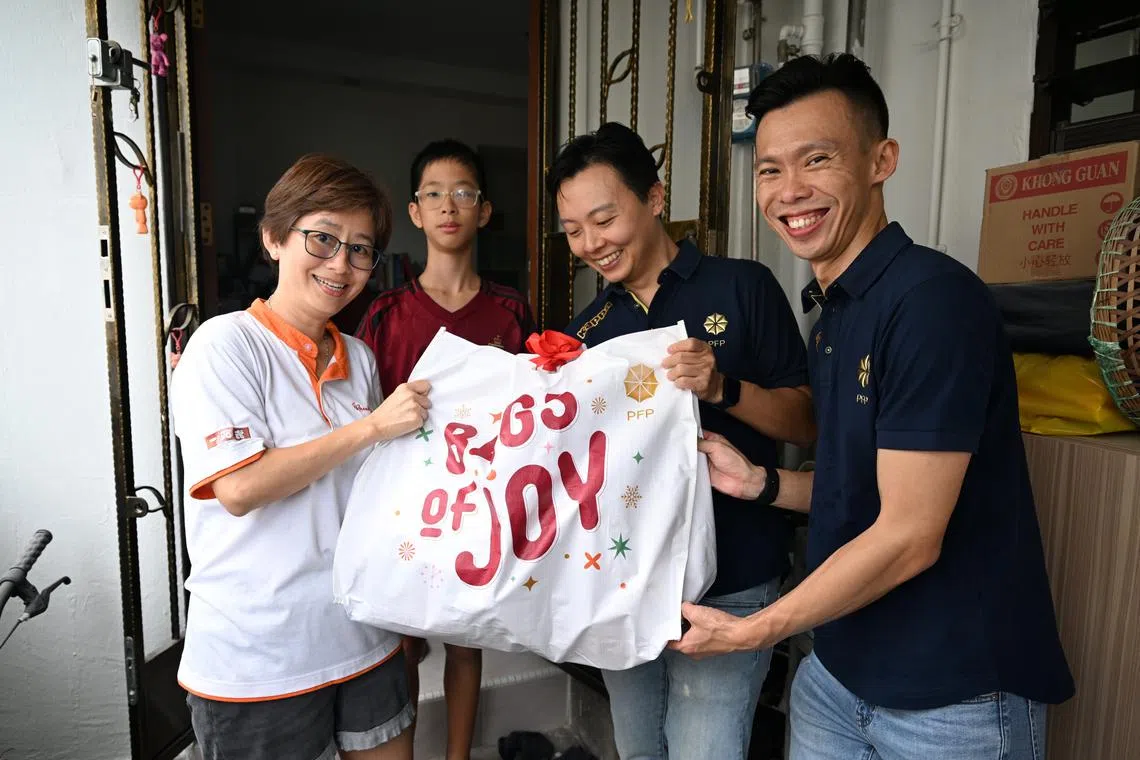 (From left) Beneficiaries Jane Lim and her son Yew Zhe Hao receiving a "bags of joy” goodie bag from financial advisors Chew Shu Xiang and Samuel Koh.
