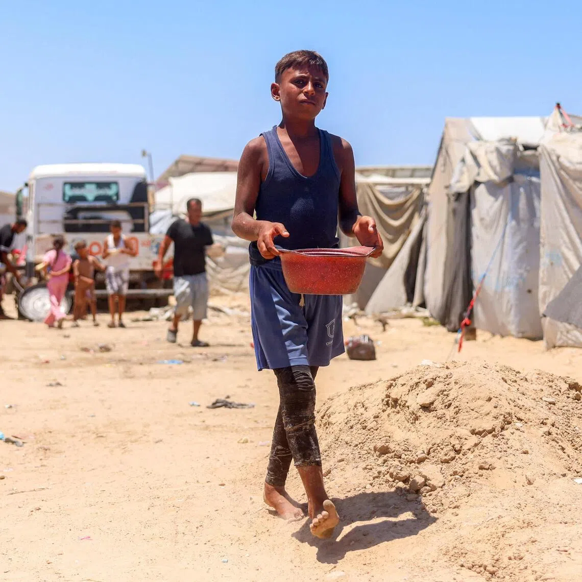 A boy walking with a pot in a camp for people displaced by war in Khan Younis in the southern Gaza Strip on July 11.