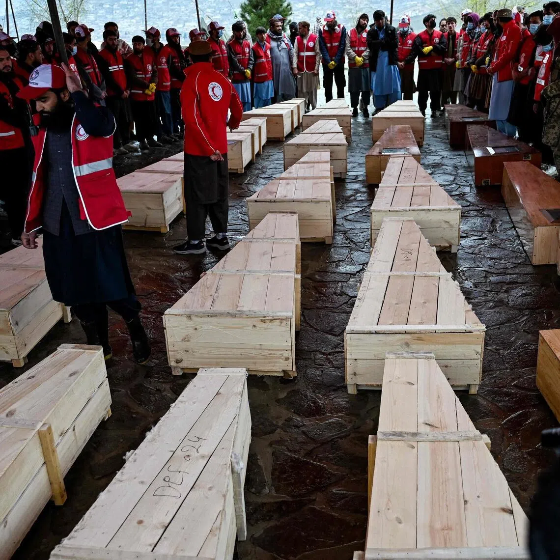 Afghan Red Crescent Society volunteers stand near the coffins of victims of a Pakistani air strike on a drug rehabilitation centre, during a mass burial at the Badam Bagh Hilltop in Kabul on March 18, 2026. 