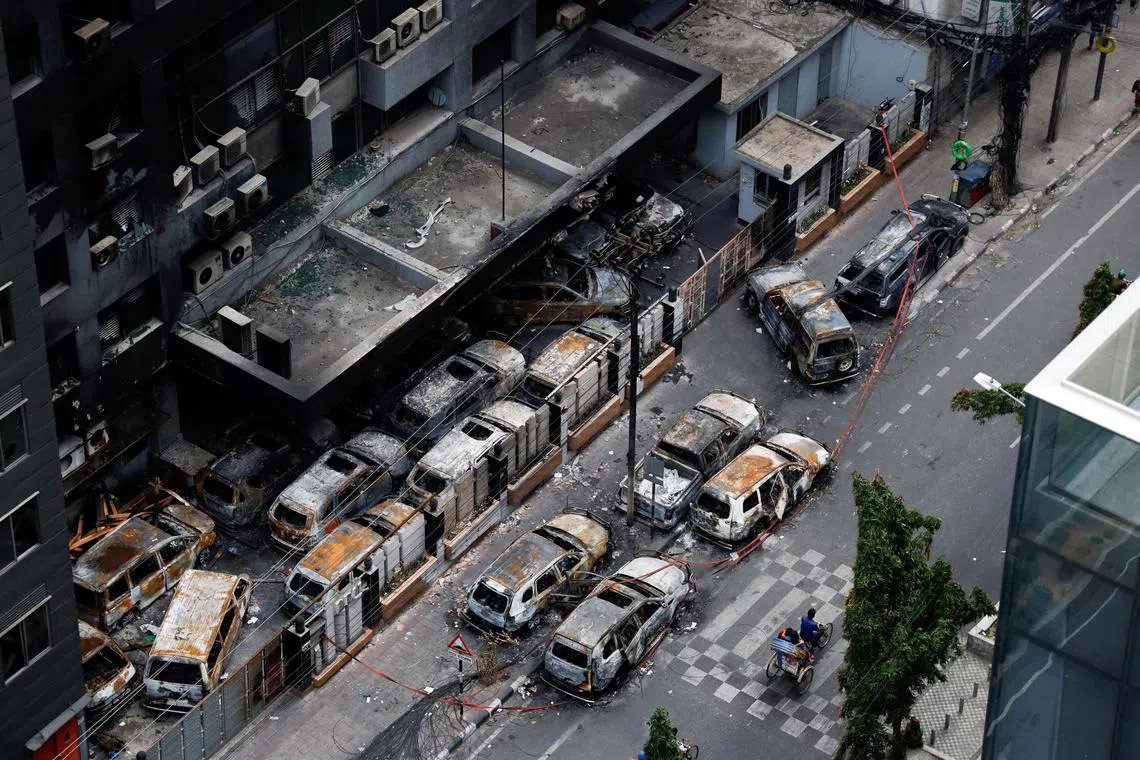 A man rides his rickshaw past damaged vehicles that were set afire by a mob during clashes after violence erupted following protests by students against government job quotas, in Dhaka, Bangladesh, July 21, 2024. REUTERS/Stringer NO RESALES. NO ARCHIVES.     TPX IMAGES OF THE DAY     