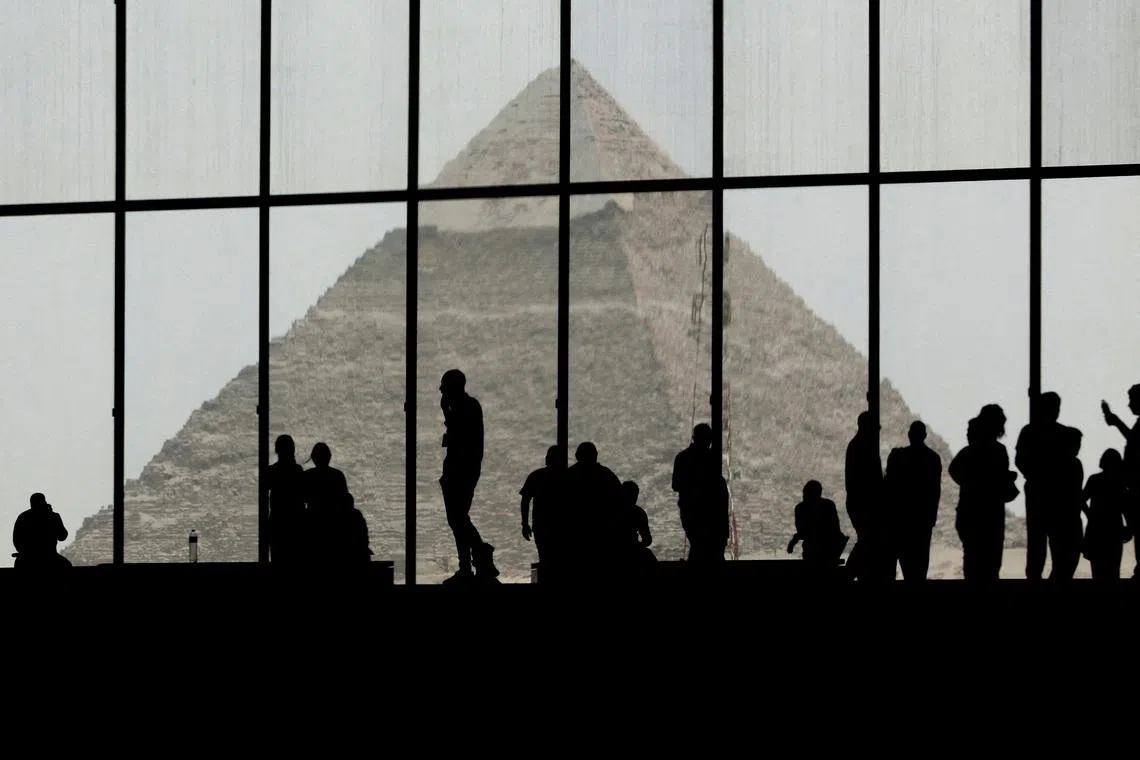 Visitors at the Grand Egyptian Museum are silhouetted against the Pyramid of Giza visible in the background, near the Giza pyramid complex, in Cairo, Egypt on May 18, 2026. 