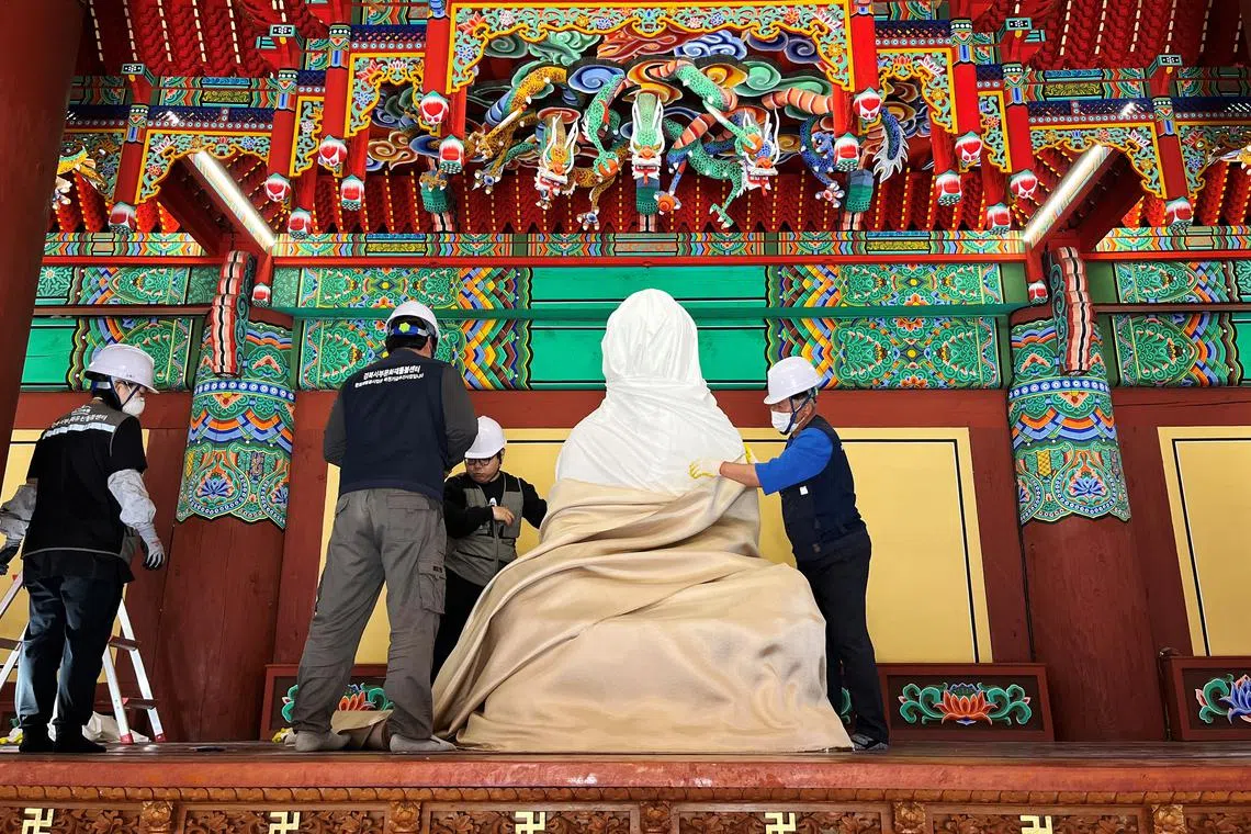 Officials wrap a Buddha statue with a fire-retardant blanket to protect it from a wildfire, at Gounsa temple in Uiseong, South Korea, March 25, 2025.  REUTERS/Minwoo Park