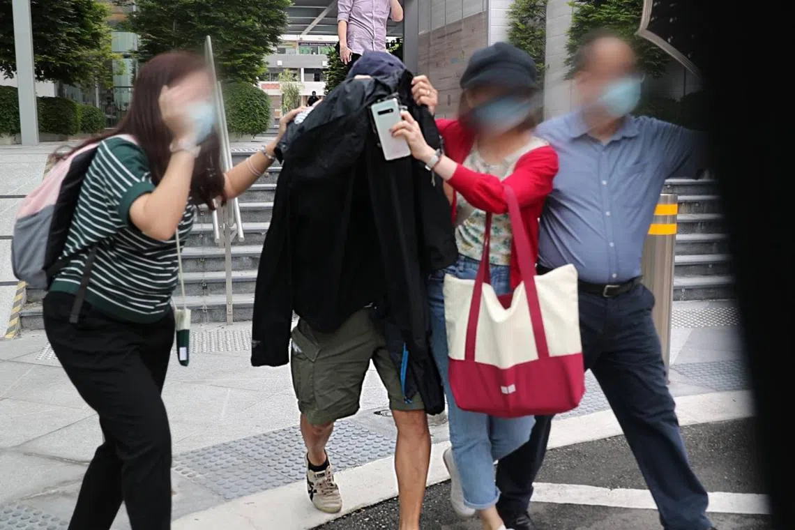 Neo Aik Chiao (centre) being ushered out at the bail exit of the State Courts on Nov 29, 2022.