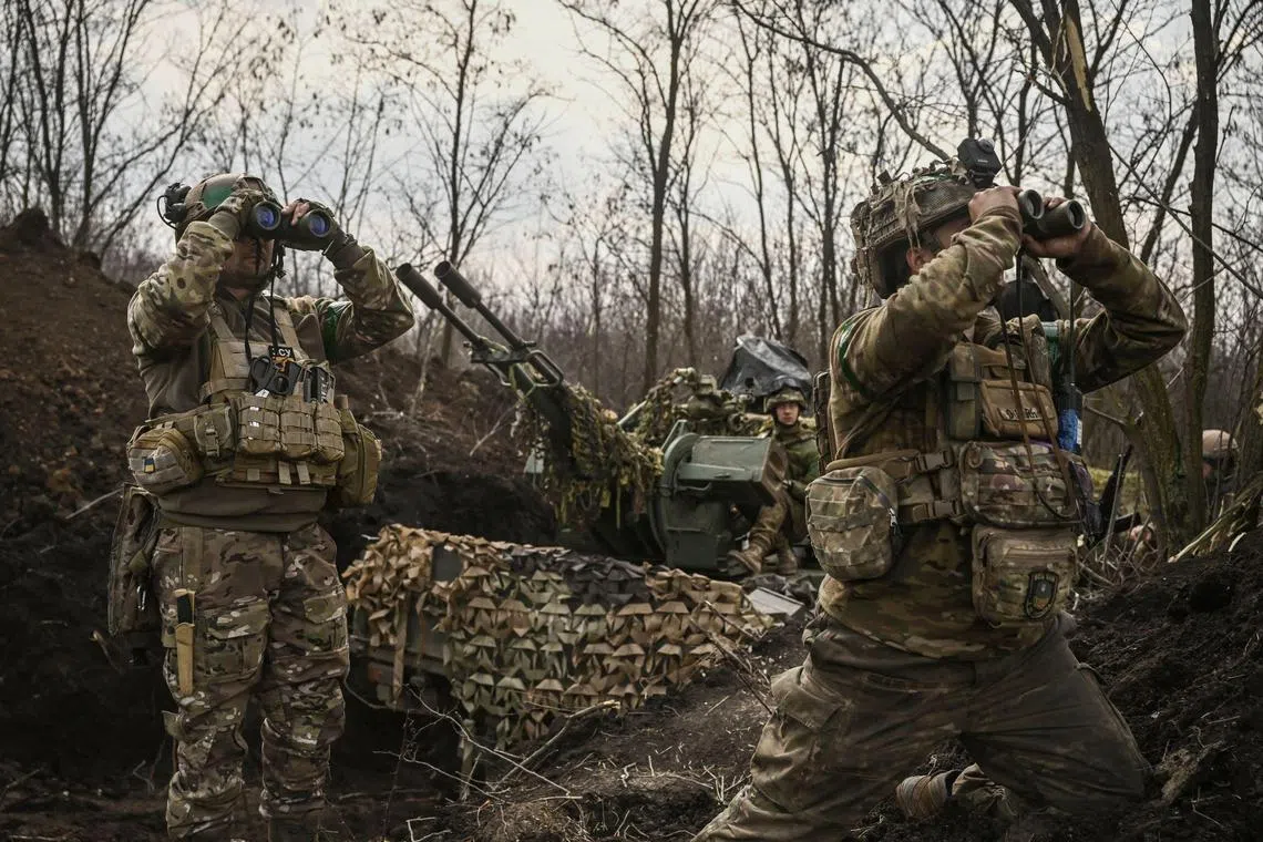 Ukrainian servicemen look on with binoculars next to another (centre) sitting on an anti-aircraft gun, near Bakhmut, on March 24, 2023. 