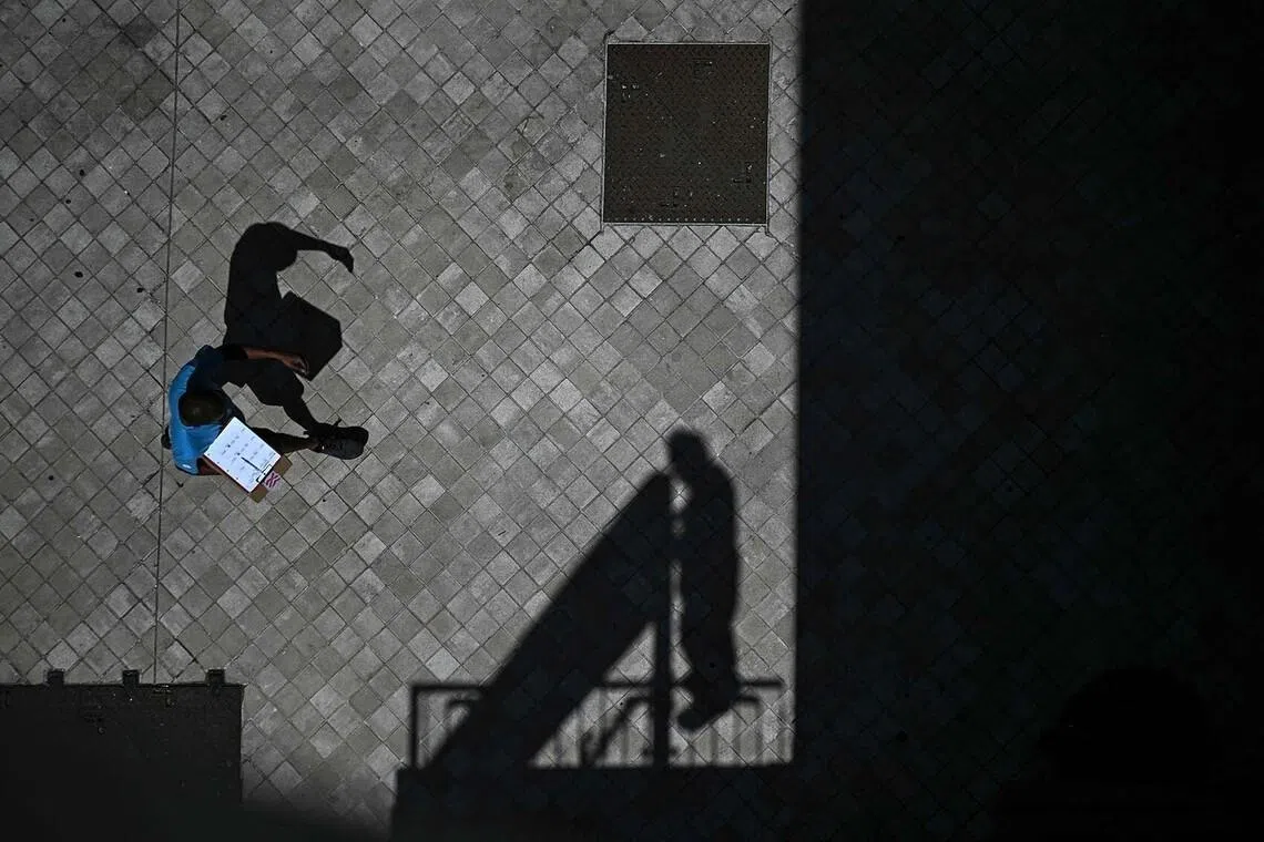 A pedestrian holding a clipboard as he walks past the shadow of a worker installing a placard at the bottom of a hotel in Bordeaux, southwestern France on June 23. 