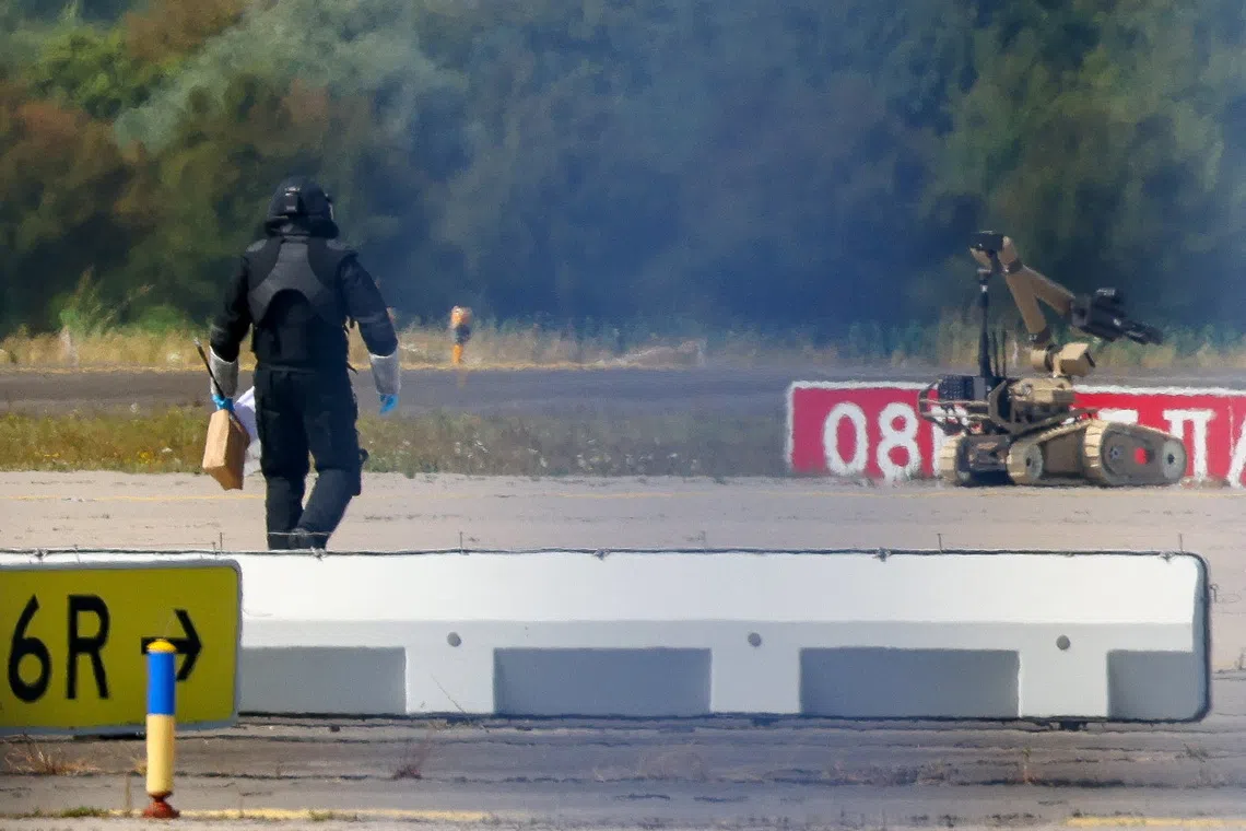 A police officer in protective clothing walks next to an explosive-disarming robot (EOD) at Leipzig/Halle Airport in Schkeuditz, Germany, August 5, 2026, after the police said explosives experts examined a drone found near a runway, and after a DHL cargo aircraft hit an unknown object as it was climbing away from the airport overnight, prompting an unscheduled landing in Hanover, according to a source familiar with the incident. REUTERS/Axel Schmidt