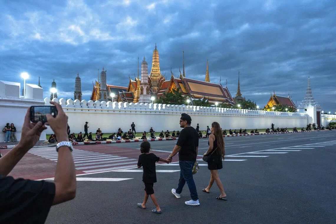 A family dressed in black crosses a street in front of the Grand Palace in Bangkok on Oct 26, 2025.