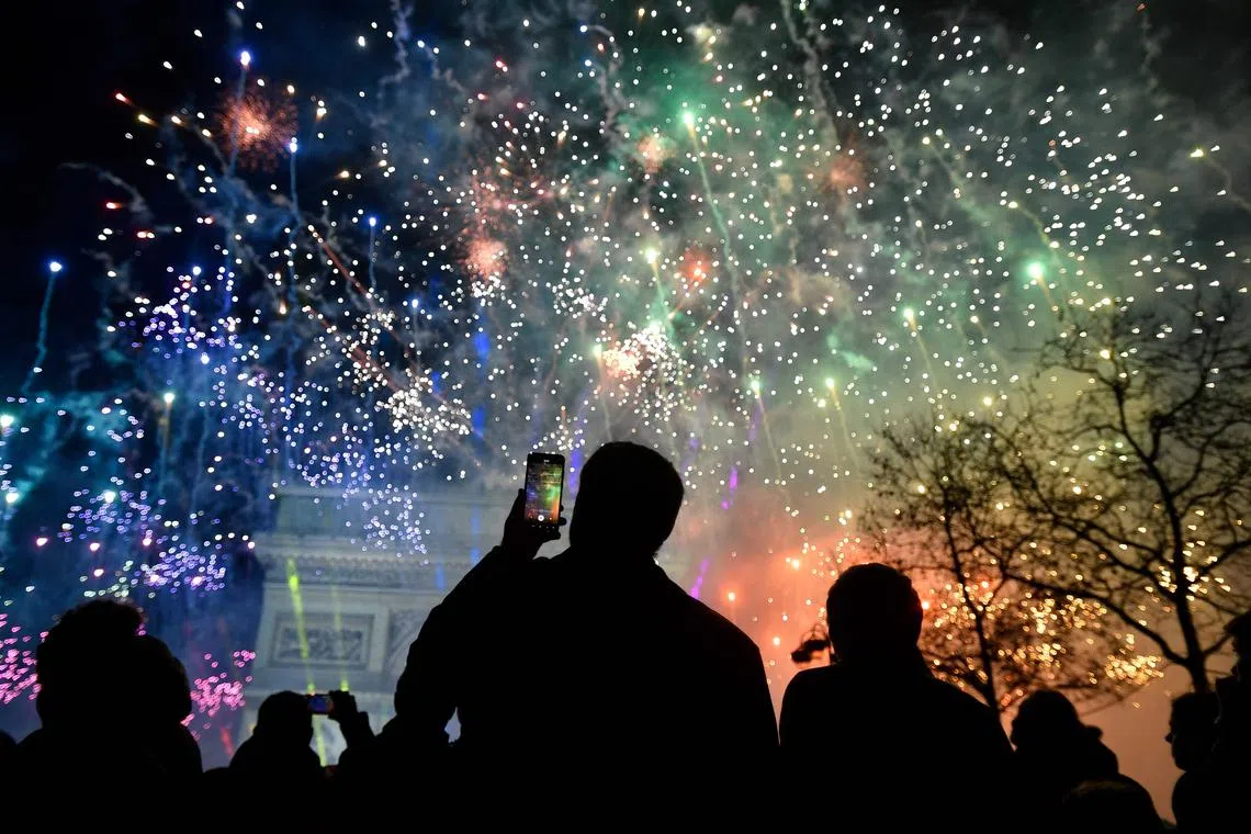 A spectator holds a smartphone as fireworks explode next to the Arc de Triomphe, at the Avenue des Champs-Elysees during New Year celebrations in Paris, early on Jan 1, 2023. 