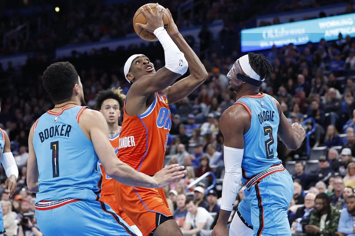 Oklahoma City Thunder guard Shai Gilgeous-Alexander driving to the basket between Phoenix Suns guard Devin Booker (No. 1) and forward Josh Okogie during the second quarter at Paycom Centre.