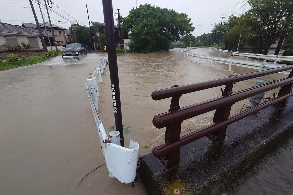 A vehilce drives along a flooded road next to the Sakai River (R), which overflowed due to the effects of Typhoon Shanshan in Tamana City, Kumamoto prefectureon on August 29, 2024. One of the strongest typhoons to hit Japan in decades dumped torrential rain across southern regions on August 29, with authorities warning of life-threatening flooding and landslides. (Photo by JIJI Press / AFP) / Japan OUT