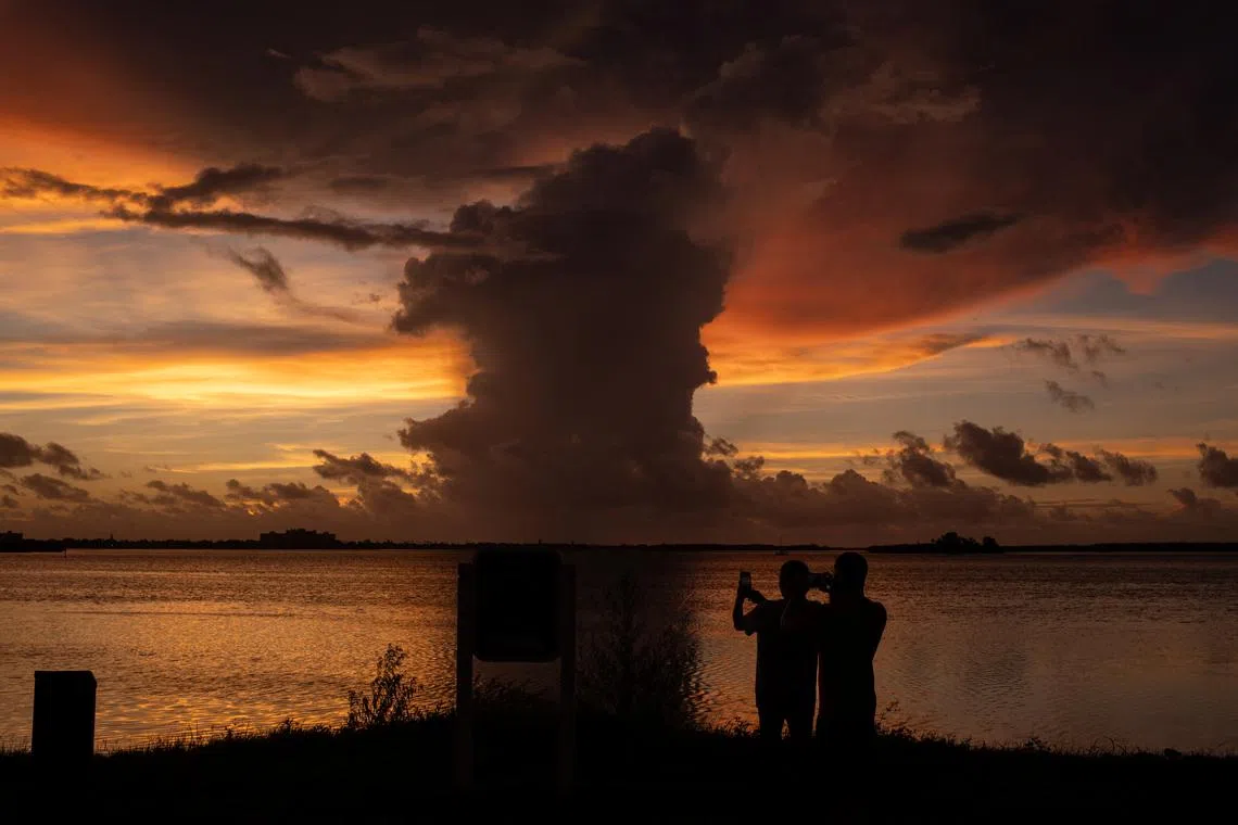Marisol Martinez and her son Jonathan Martinez photographing a cloud formation at sunset in the aftermath of Hurricane Idalia in Clearwater, Florida, U.S., Aug 30.