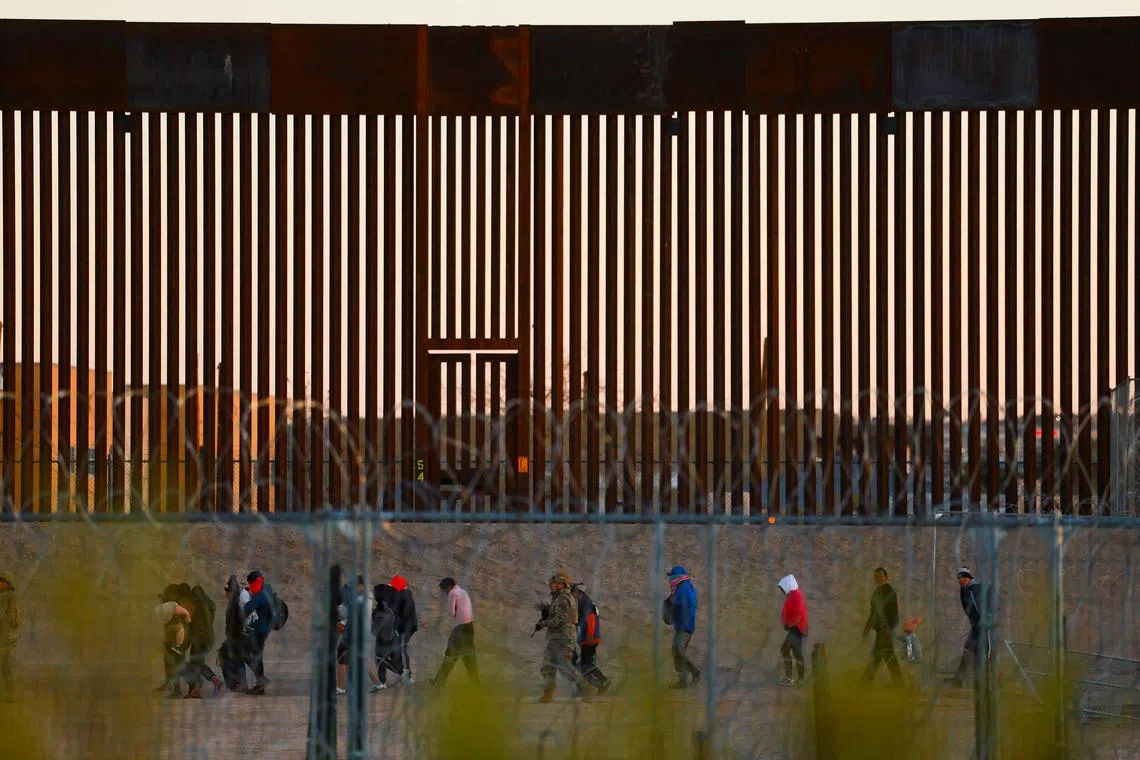 Migrants seeking asylum in the United States gather near the border wall after crossing a razor wire fence deployed to inhibit their crossing into the United States, as a member of the Texas National Guard escorts them, as seen from Ciudad Juarez, Mexico December 19, 2024. REUTERS/Jose Luis Gonzalez