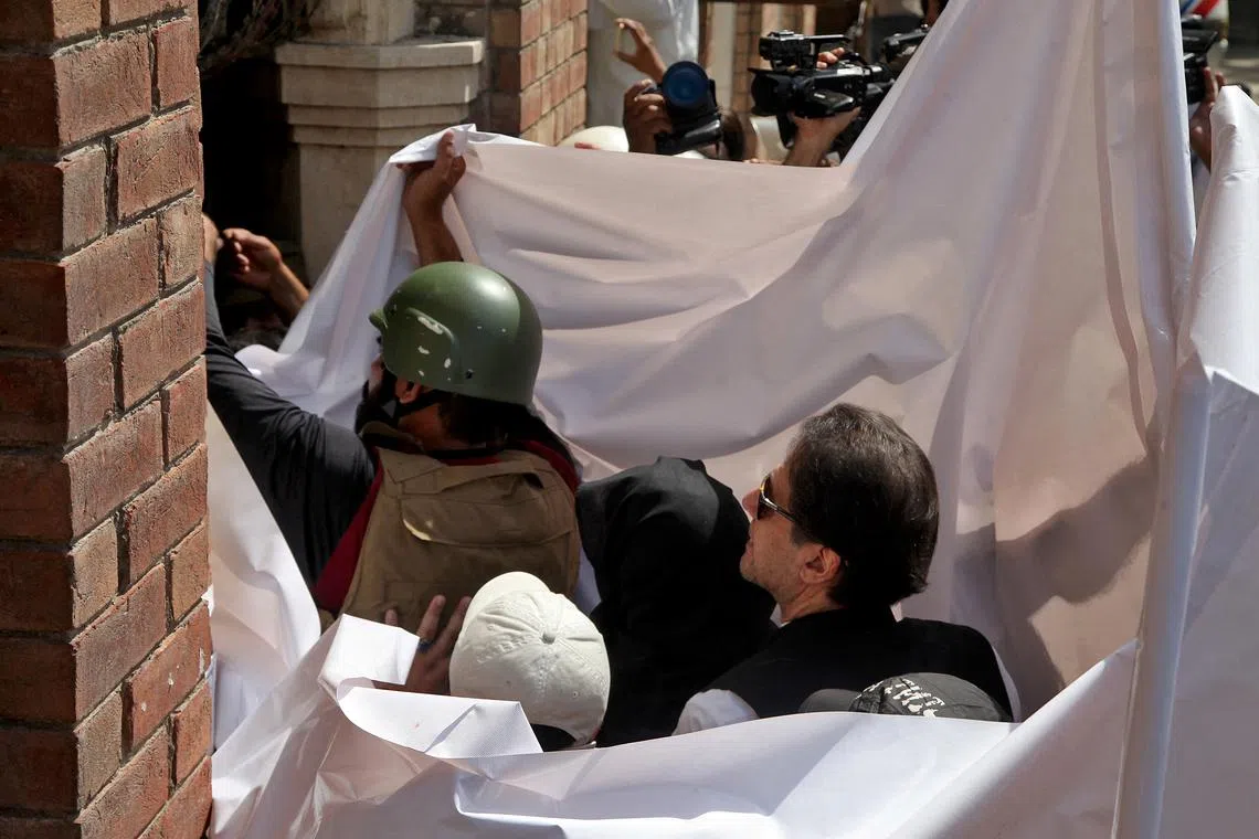 FILE PHOTO: Pakistan's former Prime Minister Imran Khan and his wife Bushra Bibi are covered with a white sheet as they arrive to appear at the High Court in Lahore, Pakistan, May 15, 2023. REUTERS/Mohsin Raza/File Photo