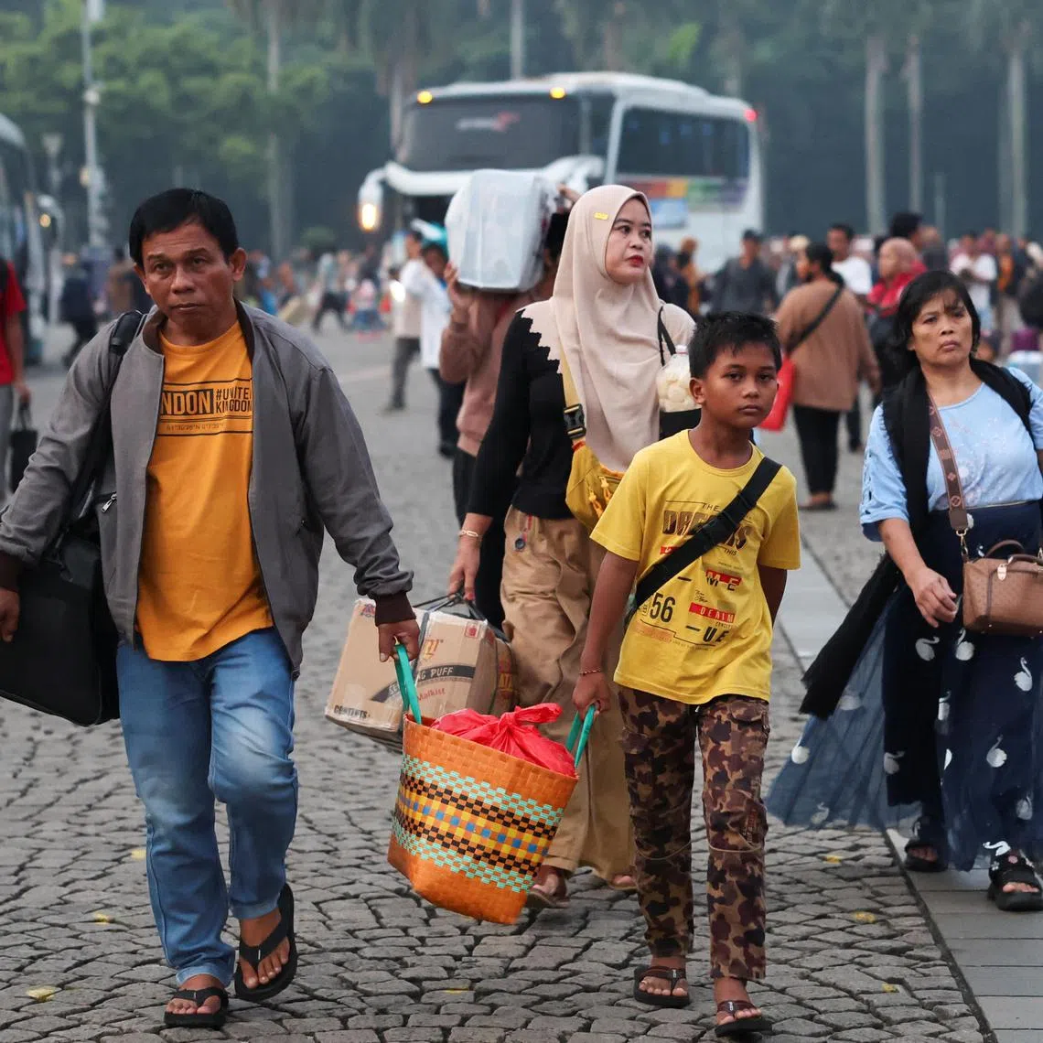 Passengers carry their luggage as people return to their hometowns, known locally as "mudik", ahead of the Eid al-Fitr celebration, at the National Monument in Jakarta, Indonesia, March 27, 2025. REUTERS/Ajeng Dinar Ulfiana