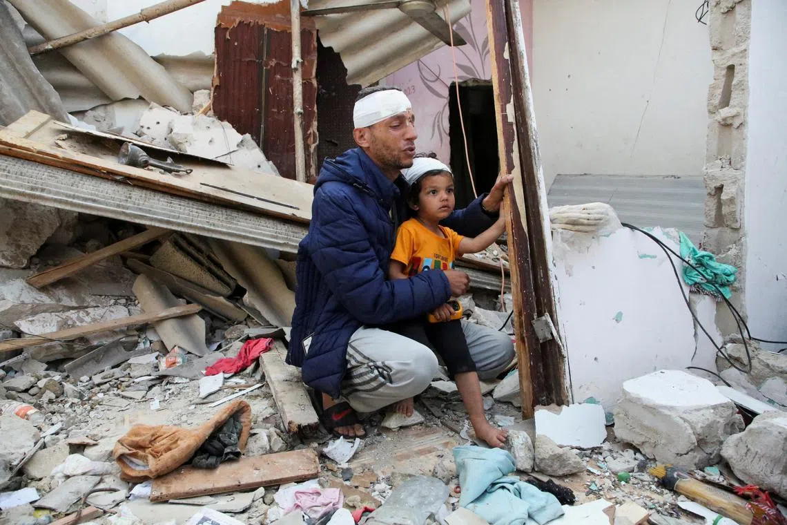 A wounded Palestinian man, carrying his injured son, reacts at the site of an Israeli strike on a house, amid the ongoing conflict between Israel and the Palestinian Islamist group Hamas, in Rafah, in the southern Gaza Strip, May 1, 2024. REUTERS/Hatem Khaled