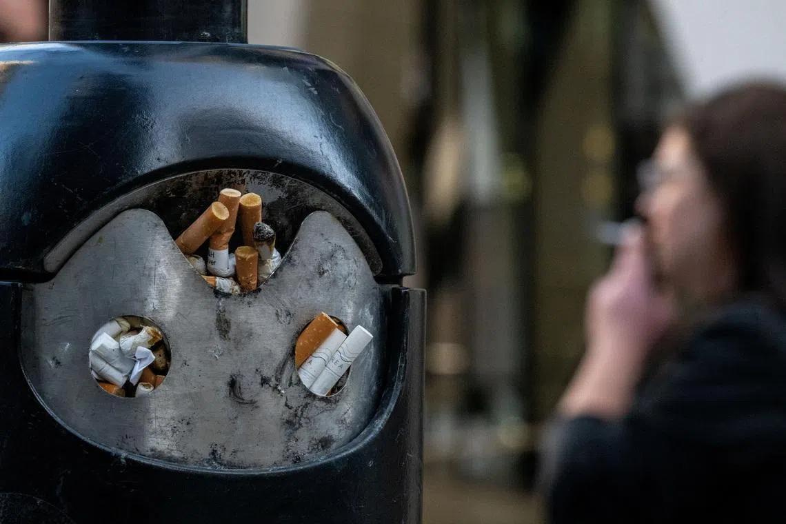 A smoker stands next to a bin for cigarette butts in London, Britain, November 26, 2024. REUTERS/Chris J. Ratcliffe