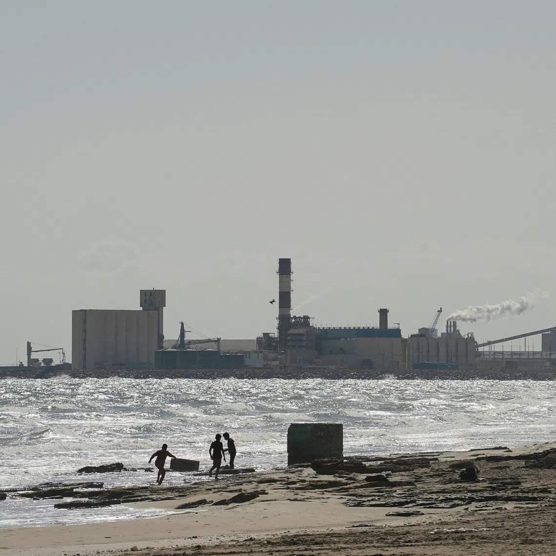 Children play on the beach with the Tunisian Chemical Group’s (CGT) phosphate complex visible in the background, in Gabes, Tunisia, October 16, 2025. REUTERS/Jihed Abidellaoui