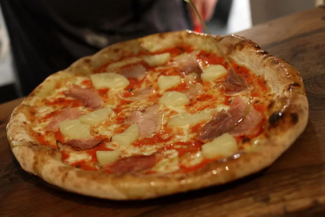 A Hawaiian, ham, and pineapple-topped pizza is prepared at Lupa Pizza restaurant in Norwich, Britain. 
