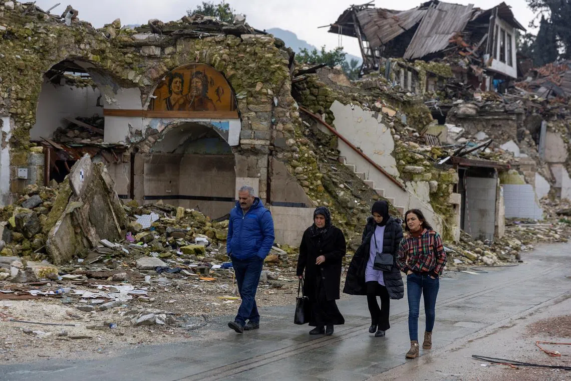 FILE PHOTO: People walk past houses destroyed by last year's earthquake, in Hatay, Turkey, February 5, 2024. The magnitude 7.8 tremor that struck in the early hours of Feb. 6, 2023, levelled towns and city swathes in the country's southeast. It killed more than 53,000 people in Turkey and nearly 6,000 in neighbouring Syria and left millions homeless. REUTERS/Umit Bektas/ File photo