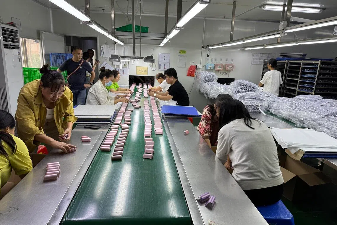 Vape shells waiting to be spray-painted and inspected by a row of workers in a small workshop in Shenzhen.