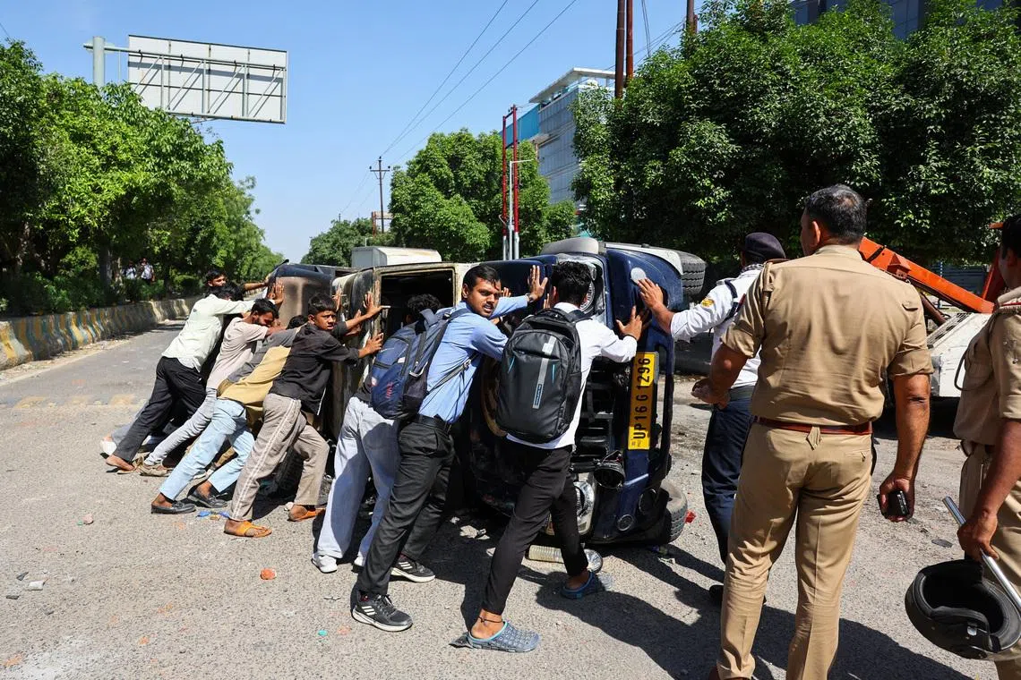 People attempting to push an overturned vehicle which was damaged during workers' protest, after factory workers demanded a wage hike amid soaring living costs, in Noida, India's industrial hub town in the state of Uttar Pradesh, on April 13. 