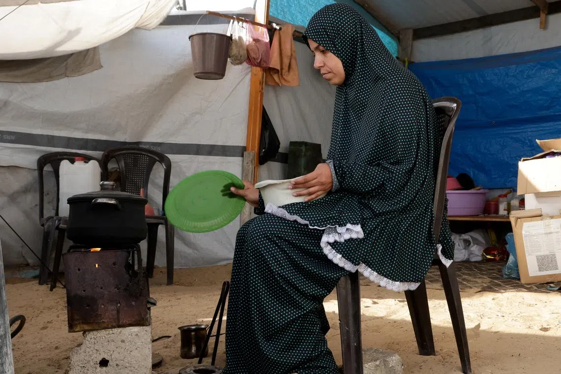 FILE PHOTO: A Palestinian woman prepares food inside her tent, in Khan Younis, in the southern Gaza Strip, May 1, 2025. REUTERS/Hatem Khaled/File Photo