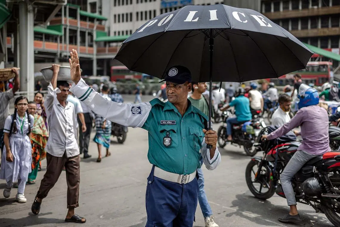 A Bangladeshi police officer holding an umbrella to protect himself from the sun while controlling the traffic at a junction after police called off their strike and resumed their duties following a meeting with the interim government in Dhaka on Aug 12, 2024. 