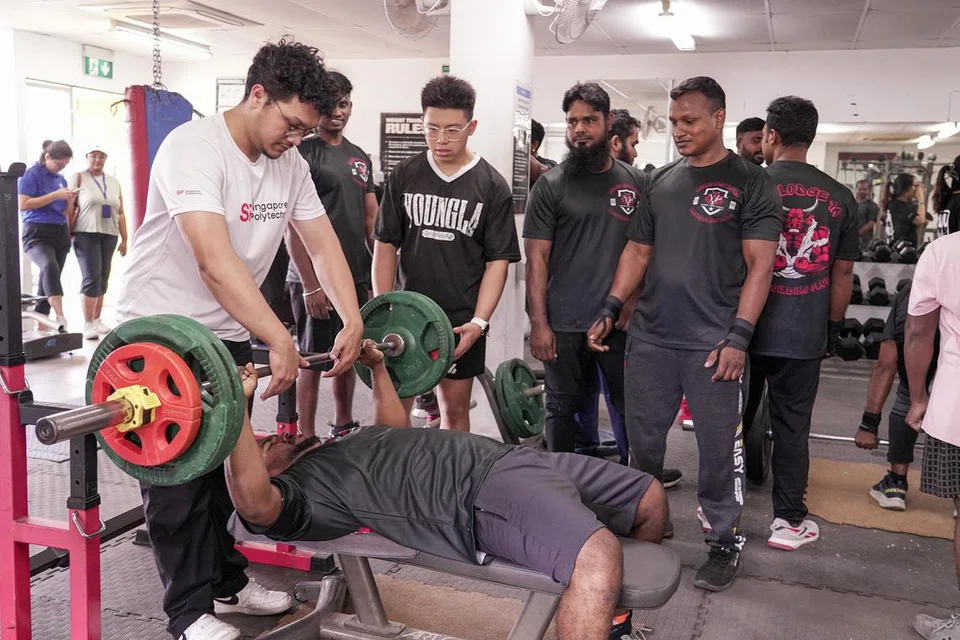 Singapore Polytechnic student Danish Irfan assisting a migrant worker during a bench press exercise.