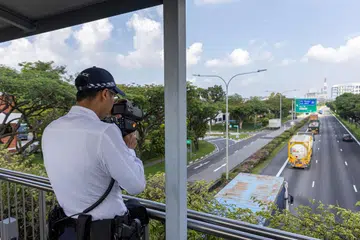 A traffic police officer using a Police Speed Laser Camera (PSLC) to detect speeding offences.