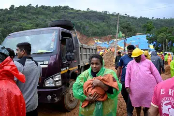 A woman holding a baby moving  to a safer place following the landslide in Wayanad district.