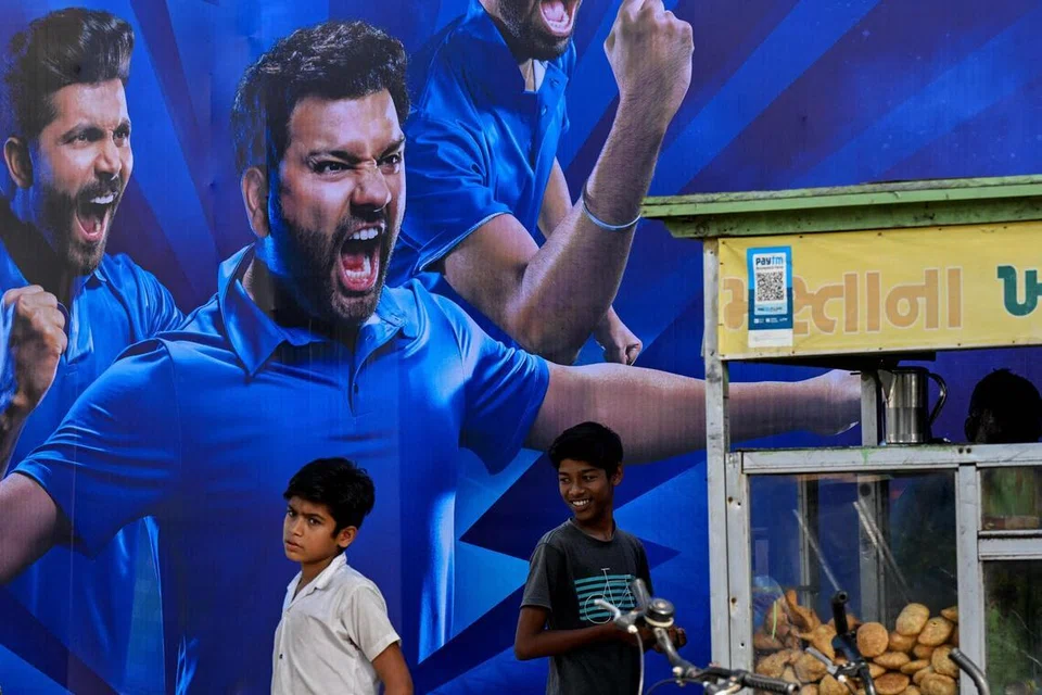 Children standing in front of a billboard displaying Indian cricketers Rohit Sharma and Ravindra Jadeja, outside Narendra Modi Stadium in Ahmedabad.