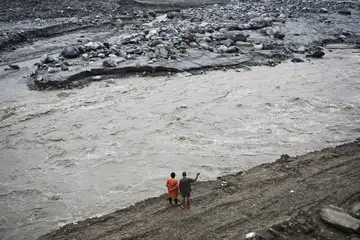 A couple stands along a river in the aftermath of the August 26 flash flood at Betrawoti Bazaar in Nepal's Nuwakot district on September 26, 2026. The August 26 flood, triggered by a glacial mountain collapse near the China-Nepal border, has killed more than 1,400 people, the majority in Nepal.
