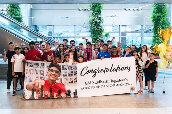 Siddharth Jagadeesh (centre with orchid lei) with his family, friends and members of the Singapore Chess Federation holding up a celebratory banner at Changi Airport.