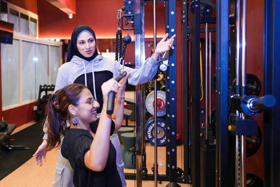 Shireen Taj guides her sister, Uzma Mueez, through an exercise at StronGirlys Gym.