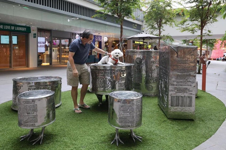 荷兰村新开张的One Holland Village是本地首家“亲宠物”商场。负责设计的本地MKPL建筑事务所先调查了解居民的需求，然后依荷兰村原有地形，将新商场有机地融入社区。商场开放式的设计，让居民可以在里头散步遛狗；走累了，还可以与宠物在餐馆或户外区进餐。这只毛孩显然很欣赏本地艺术家罗杰瀚的《罐头动物》装置艺术作品。