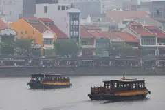 Tourist-oriented bumboats move through the Singapore River, past restaurants at Boat Quay, in haze-shrouded Singapore, October 16, 2026.