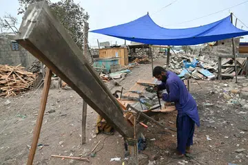 A worker building a traditional wooden boat at a yard in Ibrahim Hyderi in Karachi. The rhythmic hammering of nails and the whine of saws echo around a coastal Karachi neighbourhood, where small figures of men work atop massive wooden fishing hulls that loom beneath a pale summer sky.