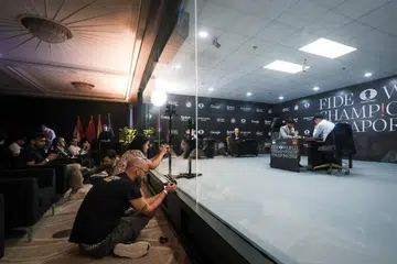 Photographers and spectators behind a one-way glass window while Gukesh Dommaraju and Ding Liren contest for the FIDE World Chess Championship at Resorts World Sentosa.