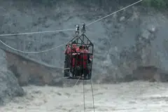 People hold onto a cage on a makeshift zip line as they cross the Trishuli River from Koloni after landslides and mudslides damaged bridges, temporarily stranding residents in Trishuli, Nuwakot district, Nepal.