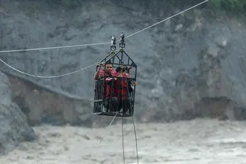 People hold onto a cage on a makeshift zip line as they cross the Trishuli River from Koloni after landslides and mudslides damaged bridges, temporarily stranding residents in Trishuli, Nuwakot district, Nepal.