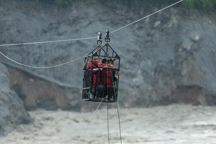 People hold onto a cage on a makeshift zip line as they cross the Trishuli River from Koloni after landslides and mudslides damaged bridges, temporarily stranding residents in Trishuli, Nuwakot district, Nepal.