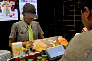 A staff takes an order as an advertisement for McDonald’s new protein slice is displayed at a McDonald’s restaurant in Bengaluru, India, on Aug 21, 2025. 