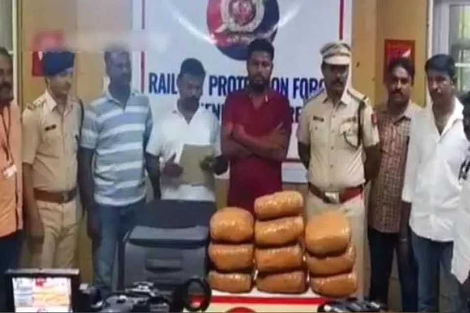 கஞ்சா மூட்டைகளைக் கடத்தி வந்த ஒடிசாவைச் சேர்ந்த இளைஞரை (சிவப்பு ஆடை) அதிகாரிகள் கைது செய்தனர்.